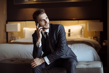 Young handsome man relaxing at his apartment in a hotel after business meeting. Business trip. Booking hotel during your vacation. Businessman in luxury room  of the expensive beautiful hotel. 