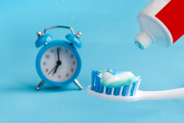 Fototapeta na wymiar Healthy teeth. Toothbrush and toothpaste and bath towel and alarm clock on the table in the bathroom blue background. Regime day, morning procedures and personal care, health care, health hygiene