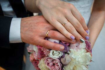 Hands of the groom and the bride with wedding rings and a wedding bouquet from roses. Two wedding rings and blossoms. Wedding concept