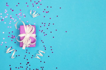 A gift box in purple wrapping paper, tied with white ribbons and decorated with a white bow, on a blue background, along with a pink one.