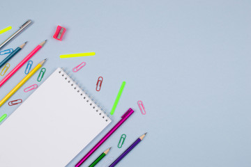 White notepad on a blue background, stationery-pencils, pens, paper clips, pencil sharpener are spread around.