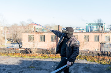 The guy in the mask, leather jacket and virtual reality glasses waving swords machete on the roof of an abandoned city building