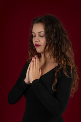 Waist up portrait of a young woman  praying with eyes closed on a dark burgundy background in the studio