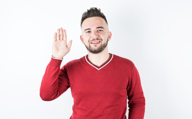 Naklejka premium Portrait of handsome young smiling man saying hi and waving with hand at camera, standing over gray background.