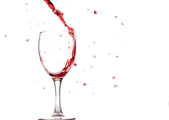 Red wine falls into a glass and creates splash and splashes on a white background.