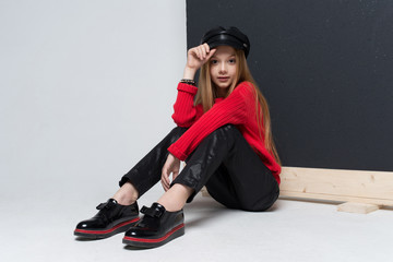 Portrait of beautiful young redhead girl wearing red sweater and black pants posing in studio.