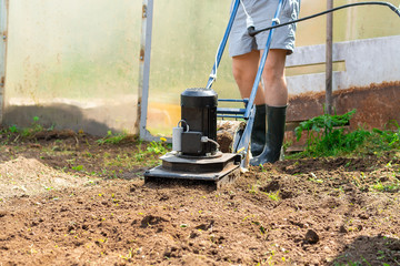 A man plows the ground in the garden with an electric cultivator