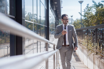 Successful businessman entering the building while holding smart phone in one hand and tablet in other.