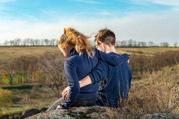 A boy and a girl are sitting on a cliff, two friends, a brother and a sister, are hugging each other.