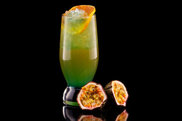 Glass of tropical cocktail with passion fruit, mango and pineapple isolated at black background.