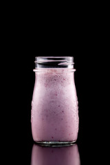 Blackcurrant smoothie in a jar isolated at black background.