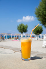 Glass of fresh orange juice on white beach sea view coast background. Relax and vacation concept.