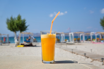 Glass of fresh orange juice on white beach sea view coast background. Relax and vacation concept.