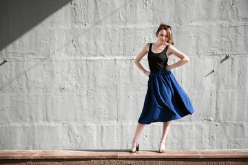 young girl posing against a concrete wall, dressed in black, hard light and shadows