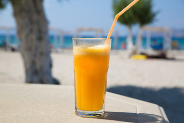Glass of fresh orange juice on white beach sea view coast background. Relax and vacation concept.