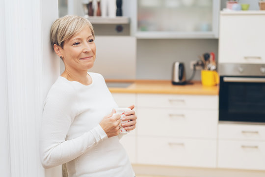 Woman standing in her kitchen drinking coffee