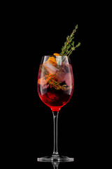 Glass of red sangria wine cocktail decorated with thyme and orange isolated at black background.