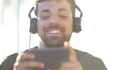 Millenial young man using his smartphone for listening music with headphones