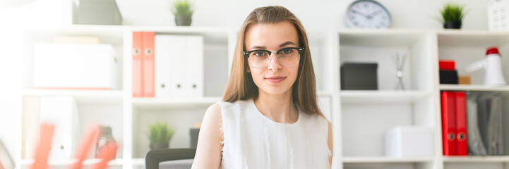 Fototapeta premium Beautiful young girl is sitting at the table in the office, holding a pen in her hand and filling out the documents.