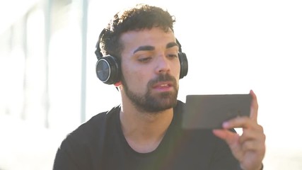 Millenial young man using his smartphone for listening music with headphones
