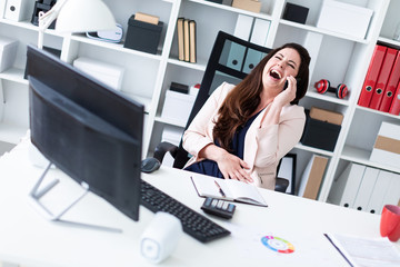 A young girl sitting at an old computer, talking on the phone and laughing.