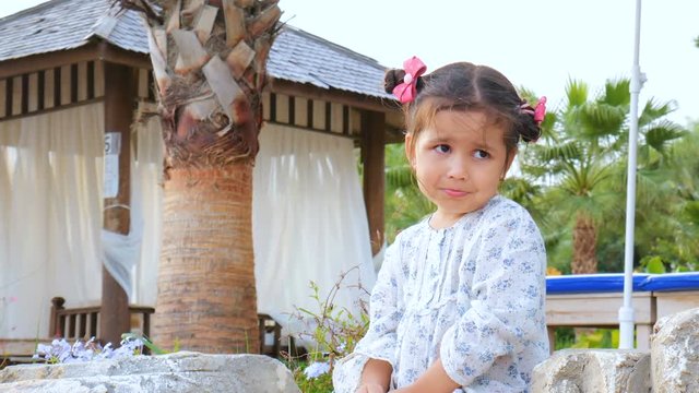 Little actress with a good imagination. Cute beautiful baby girl talking to herself, sitting on the beach under palm trees next to the gazebo.