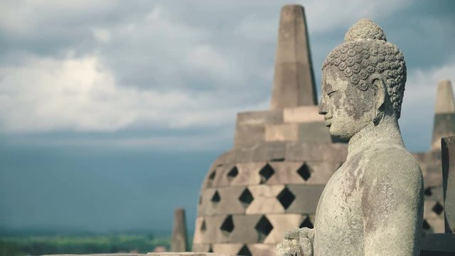 Close up Buddha stone statue and stupa on top of Borobudur temple in Java, Indonesia on sunny evening, slide right
