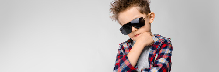 A handsome boy in a plaid shirt, gray shirt and jeans stands on a gray background. The boy in black...