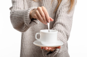 Young woman in sweater holding a white cup and saucer in hands, drinking hot coffee on white background. Space for your logo or text.