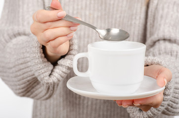 Fototapeta na wymiar Young woman in sweater holding a white cup and saucer in hands, drinking hot coffee on white background. Space for your logo or text.