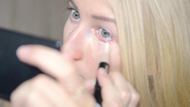 beautiful blonde girl looks in the mirror and paints eyes
