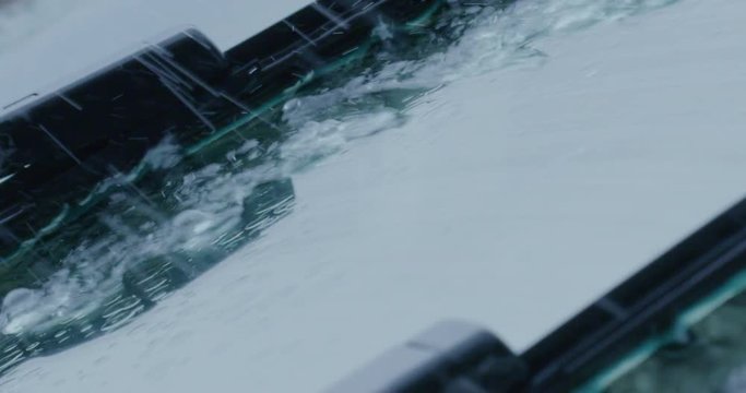 Super close up of a carglass while it&rsquo;s raining, the wipers are taking off the water from it. Concept: thunderstorm, car, weather. Shot on Red Camera 8K