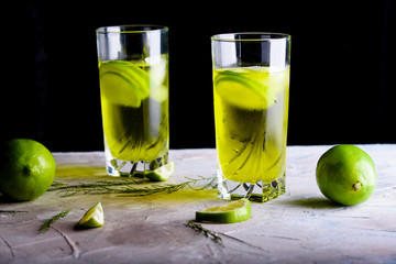 Delicious yellow drink with a handful of green lemon. Cocktail with limnom concrete background. Yellow cocktail with lemon.