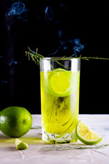 Delicious yellow drink with a handful of green lemon. Cocktail with limnom concrete background. Yellow cocktail with lemon.