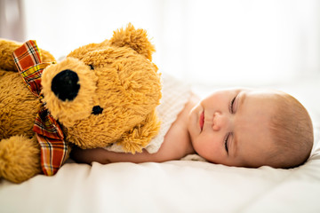 A 4 month baby sleeping on a white bed at home with bear