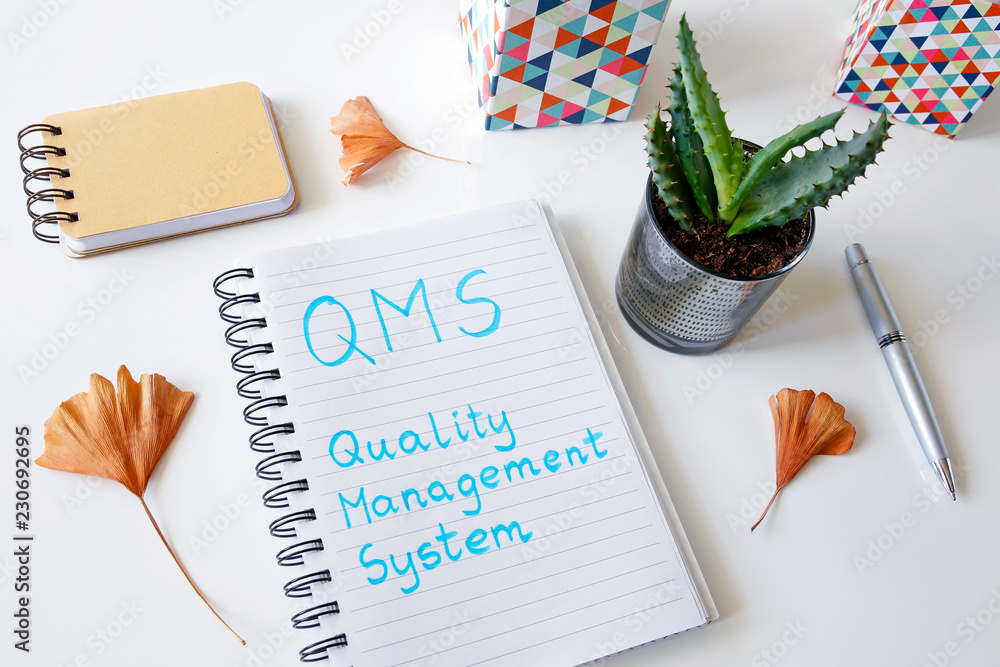 Poster qms quality management system written in a notebook on white table