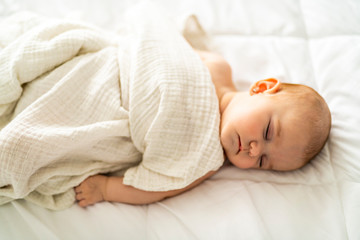 A 4 month baby sleeping on a white bed at home