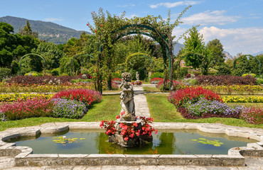 Giardino fiorito con fontane, archi, aiuole e colline sullo sfondo, Villa Pallavicino, Stresa, Lago Maggiore, Italia - obrazy, fototapety, plakaty