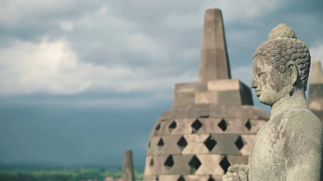 Close up Buddha stone statue and stupa on top of Borobudur temple in Java, Indonesia on sunny evening, slide right