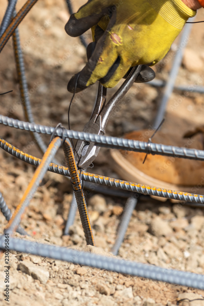 Wall mural Worker Securing Steel Rebar Framing With Wire Plier Cutter Tool At Construction Site