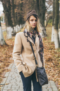 Stylish teen girl in a coat and hat stands on the street in the autumn. Attractive young woman in fashionable clothes.