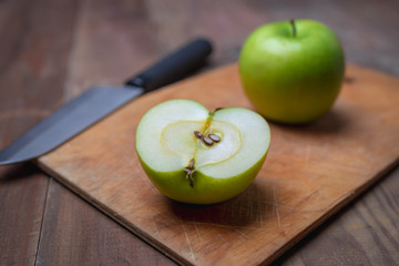 Green apple with knife on wooden cutting board