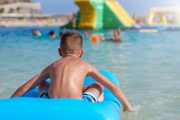 Portrait of happy Caucasian boy having fun with inflatable mattress in swimming pool at resort. Back view.