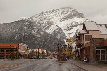  Street view of snowcapped Cascade mountain from the downtown street in the city of Banff in late fall, wet pavement under a cloudy sky, Banff National Park