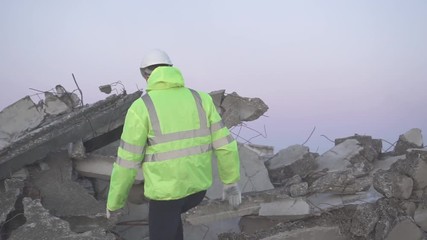 a rescuer in a signal vest after an earthquake sneaks around a destroyed house