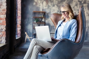 Image of cheerful office woman with blond hair in business wear sitting on chair and working with...