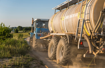A blue tractor with a tank rides along a road in a wheat field.