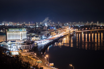 Fototapeta premium Panorama of night city landscape with river and bridge. Reflection of glowing lanterns in water.