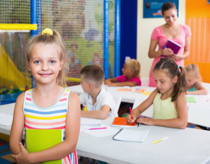 Smiling junior girl standing with textbook in school