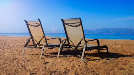 Two wooden sun loungers stand on the Adriatic Sea coast under dramatic cloudy sky